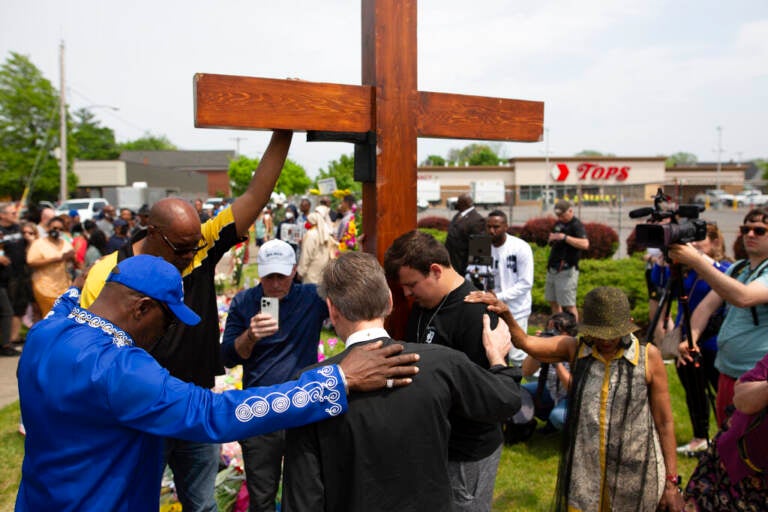 A group of mourners gather in front of a cross.