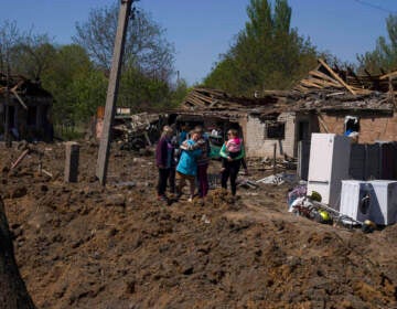 People react as they stand next to a crater in destroyed residential area after Russian airstrike in Bakhmut, Donetsk region, Ukraine, Saturday, May 7, 2022.