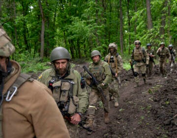 Ukrainian servicemen walk in the forest near a recently retaken village, north of Kharkiv, east Ukraine, Sunday, May 15, 2022.