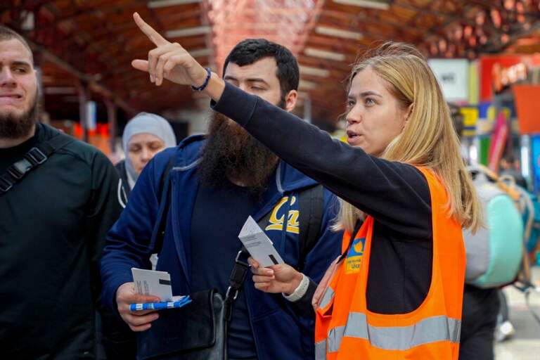 A Urkrainian volunteer wearing an orange vest gestures in the distance as she stands next to a group of people.