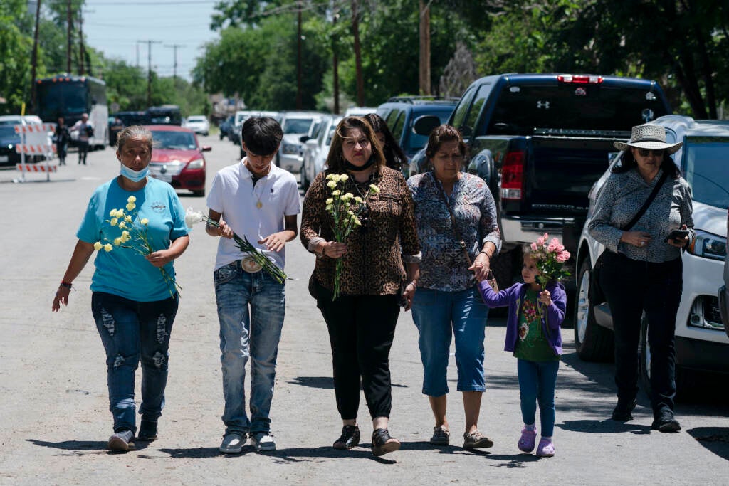 People walk with flowers to honor the victims of the Uvalde mass shooting