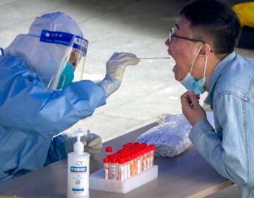 A worker in a protective suit swabs a man's throat for a COVID-19 test at a testing site in an office complex in Beijing, Friday, April 29, 2022. The World Health Organization on Thursday, May 5, 2022 is estimating that nearly 15 million people were killed either by the coronavirus or by its impact on overwhelmed health systems in the past two years, more than double the official death toll of 6 million.