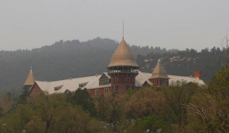 The United World College of the American West sits empty of students but unharmed, while trees can be seen behind it scorched from Las Vegas, N.M., on Saturday, May 7, 2022. School officials were able to visit the grounds earlier this week after winds and fires waned. Students at the boarding school most of whom are from overseas, have been moved to a summer camp outside Santa Fe, N.M.