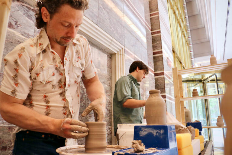 Benjamin Peterson (left) and Mike Sullivan throw clay in the lobby of 3 Logan Square in Center City. Over the course of seven weeks, they will create 156 handmade clay bottles as their contribution to the Plastic-free Philly campaign. (Emma Lee/WHYY)