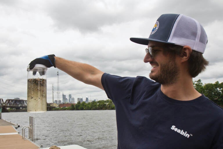 Hayden Gould, Executive Project  Manager, Seabin North America, holds up a container of micro plastics collected out of the Delaware River Watershed at a demonstration of their trash collecting devices at Bartrams’ Gardens on June 7, 2022. (Kimberly Paynter/WHYY)
