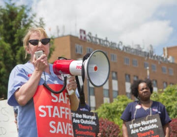 Maureen May holds a protest sign and speaker at a protest outside Suburban Community Hospital