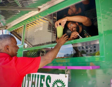 Victor Cobbs of The Green Machine food truck serves up a smoothie to Camden Mayor Vic Carstarphen. Food truck vendors can apply for seven licenses to operate in select locations under the city's pilot program. (Emma Lee/WHYY)