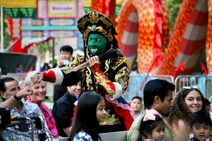 A face-changing performer, with a green mask on, fist bumps someone in the crowd around them.