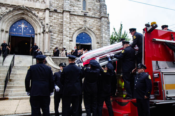 Officers carry a casket draped with the American flag down from a fire truck, with the church in the background.