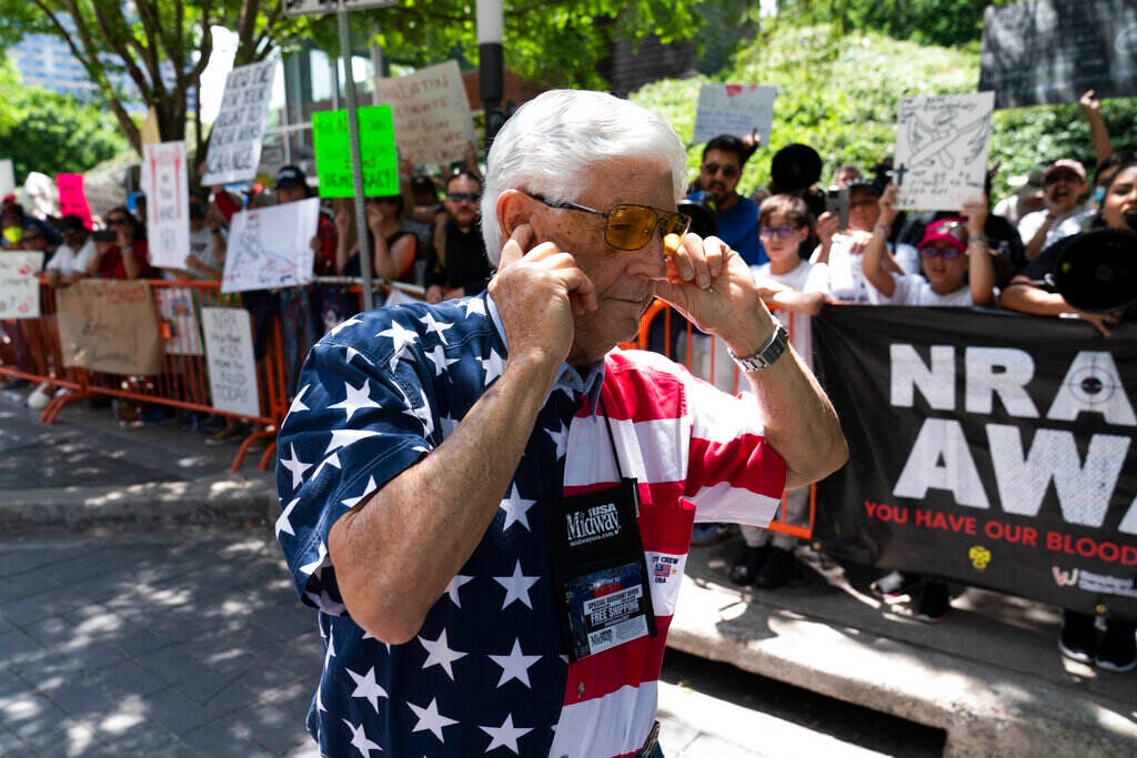 A member of the National Rifle Association plugs his ears with his fingers as he walks past protesters during the NRA's annual meeting at the George R. Brown Convention Center