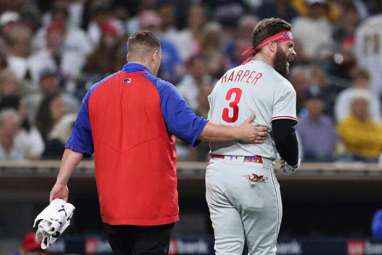 Philadelphia Phillies' Bryce Harper, right, reacts towards San Diego Padres' Blake Snell after being hit by a pitch from Snell, as he walks off the field with a trainer during the fourth inning of a baseball game Saturday, June 25, 2022, in San Diego. (AP Photo/Derrick Tuskan)