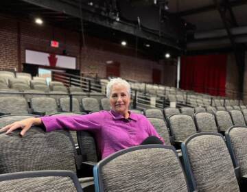 Carmen Khan sits in the middle of the audience seats of a theater, with her arm stretched out over the chair next to her.