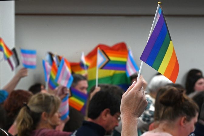 Audience members wave pride flags while a parent speaks during the public comment period of a Central Bucks School District meeting