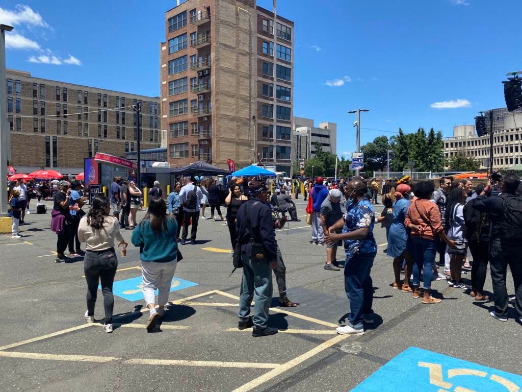 View of a crowd of people dancing in an open space with buildings in the background.