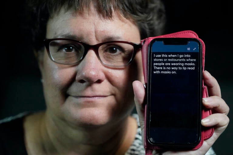 Chelle Wyatt holds up a cell phone displaying the Otter app, with a message that reads, ''I use this when I go into stores or restaurants where people are wearing masks. There is no way to lip read with masks on.''