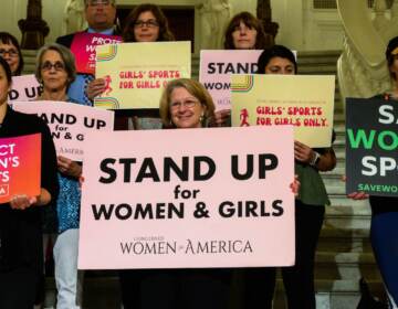 Supports of Pa. legislation that would ban trans student athletes from participating on teams corresponding with their gender hold up signs that say, ''Stand up for women and girls''