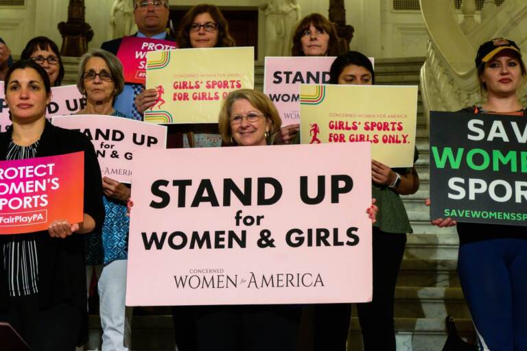 Supports of Pa. legislation that would ban trans student athletes from participating on teams corresponding with their gender hold up signs that say, ''Stand up for women and girls''