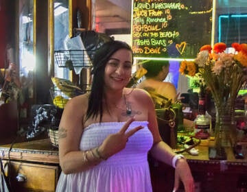 Una bartender se inclina en el bar, mostrando el signo de la paz.