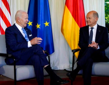 President Biden sits in a chair on the left, with Germany's Chancellor Olaf Scholz sits in a chair on the right, appearing to be listening to President Biden as he talks.