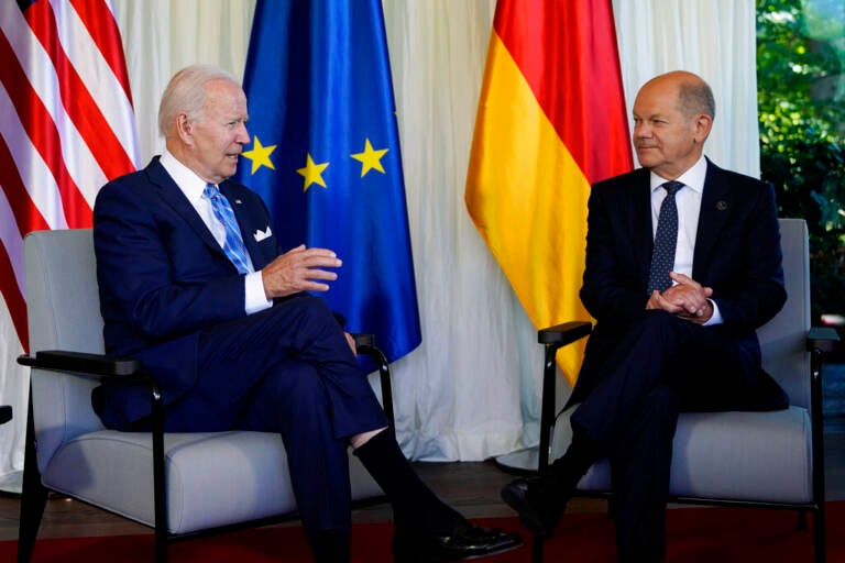 President Biden sits in a chair on the left, with Germany's Chancellor Olaf Scholz sits in a chair on the right, appearing to be listening to President Biden as he talks.