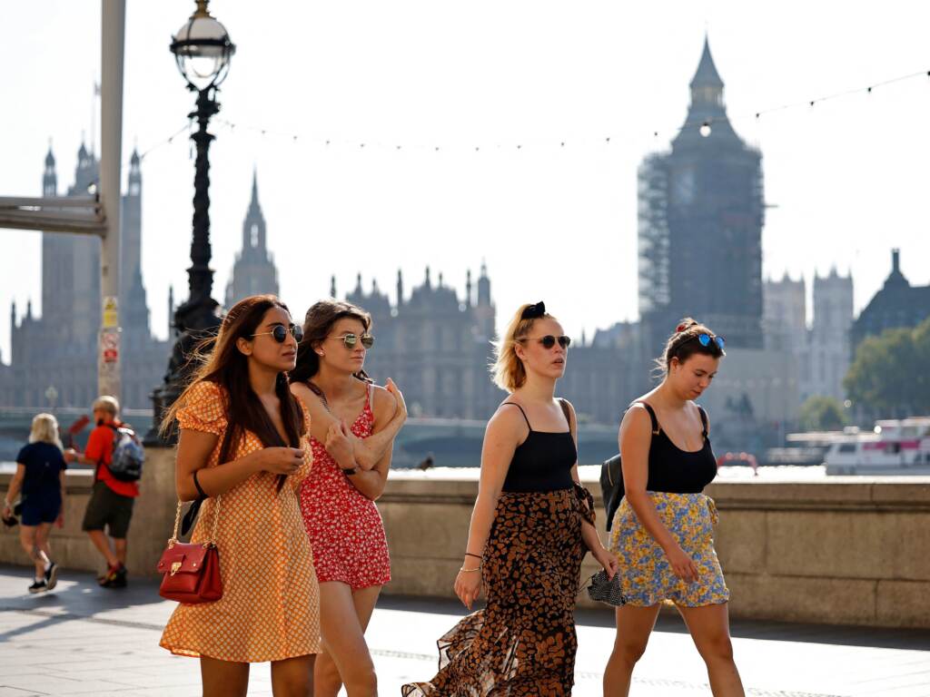 Pedestrians walk in the sunshine along the south bank of the River Thames