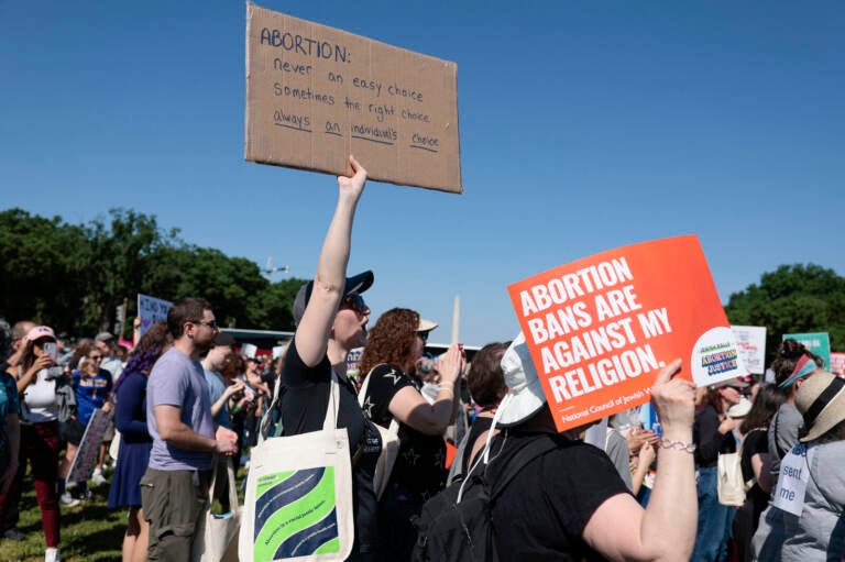 A protester holds up a sign supporting abortion rights in the midst of a crowd, with a blue sky in the background.