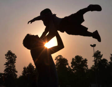 A silhouette of a father throwing his child up in the air.