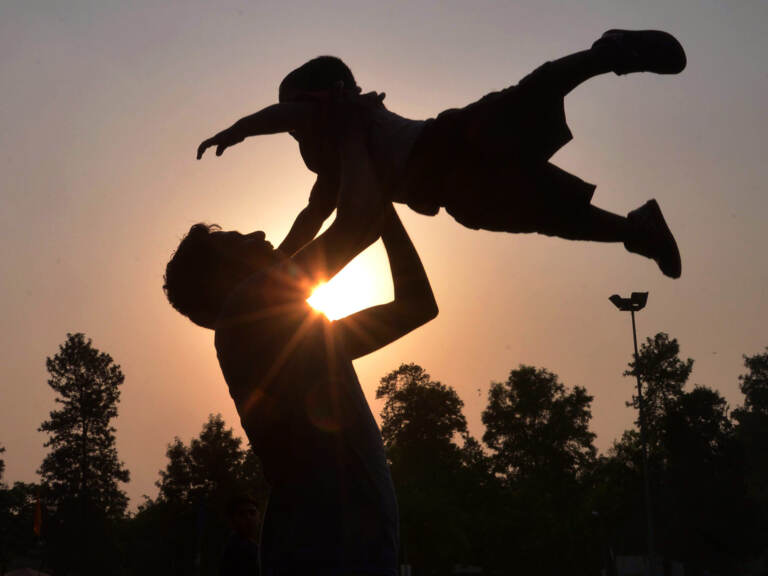 A silhouette of a father throwing his child up in the air.