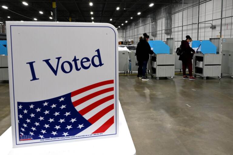 An ''I Voted'' decal is seen in the foreground, as voters cast their ballots in the background