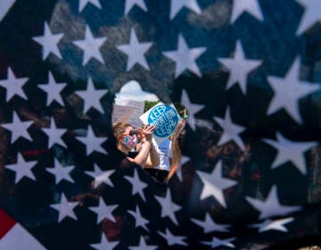 Abortion-rights activists are seen through a hole in an American flag as they protest outside the Supreme Court