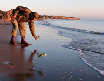 A WWII soldier re-enactor picks something up on the beach in Normandy.