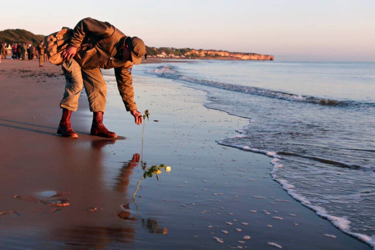 A WWII soldier re-enactor picks something up on the beach in Normandy.