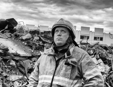 A man in a firefighter suit looks up toward the sky. The photo is in black and white.