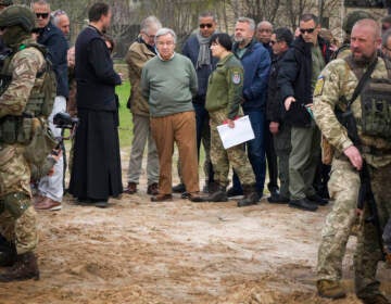 File photo: U.N. Secretary-General Antonio Guterres, center, stands on the side of a mass grave in Bucha, on the outskirts of Kyiv, Ukraine, Thursday, April 28, 2022. Police are investigating the killings of more than 12,000 Ukrainians nationwide in the war Russia is waging, the national police chief said Monday. In the Kyiv region near Bucha, authorities showed several victims whose hands were tied behind their backs.