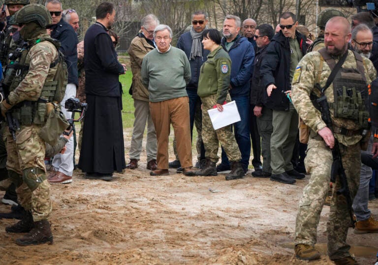 File photo: U.N. Secretary-General Antonio Guterres, center, stands on the side of a mass grave in Bucha, on the outskirts of Kyiv, Ukraine, Thursday, April 28, 2022. Police are investigating the killings of more than 12,000 Ukrainians nationwide in the war Russia is waging, the national police chief said Monday. In the Kyiv region near Bucha, authorities showed several victims whose hands were tied behind their backs.