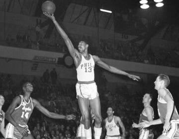 Wilt Chamberlain stretches up to make a basket in a black-and-white photo from 1961.