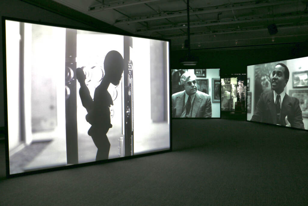 A video panel shows an African art figure under glass, with other video panels in the background showing Albert Barnes and Alain Locke.