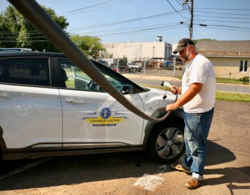Andrew Krauss charges an electric vehicle, with the road visible in the background.