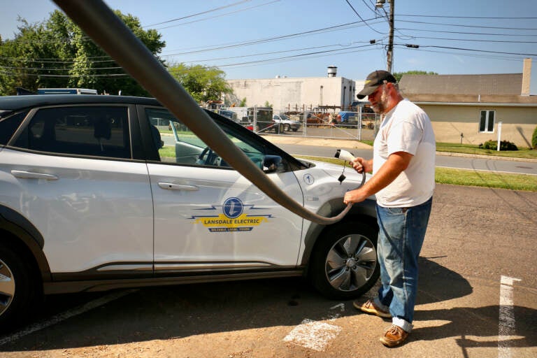Andrew Krauss charges an electric vehicle, with the road visible in the background.