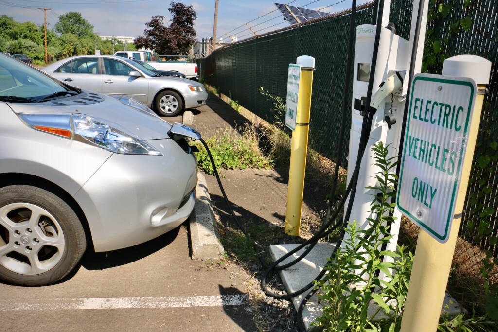 An electric charge is plugged into a charging station, next to a sign that reads, "Electric Vehicles only."