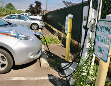 An electric charge is plugged into a charging station, next to a sign that reads, 