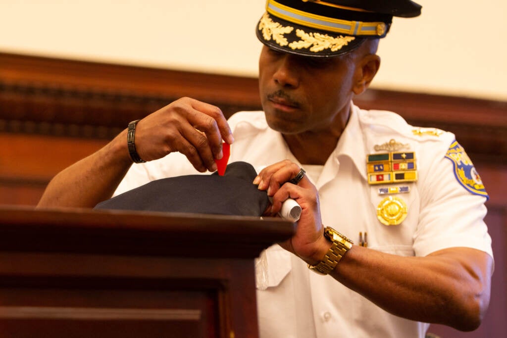 Deputy Commissioner Joel Dales points to a bullet hole in the hat of Officer Sergio Diggs