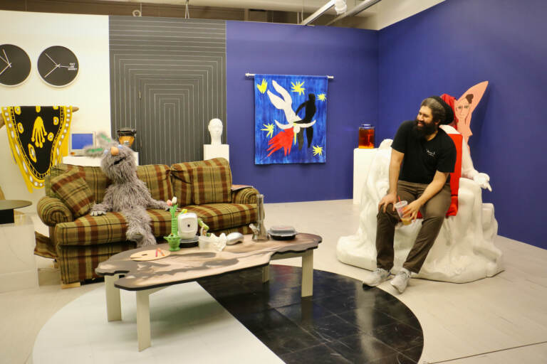 Jasson Musson sits on his ''Pieta'' chair on a stage set filled with art allusions and an animatronic puppet named Ollie. The set was used to create Musson's satiric art history videos. (Emma Lee/WHYY)