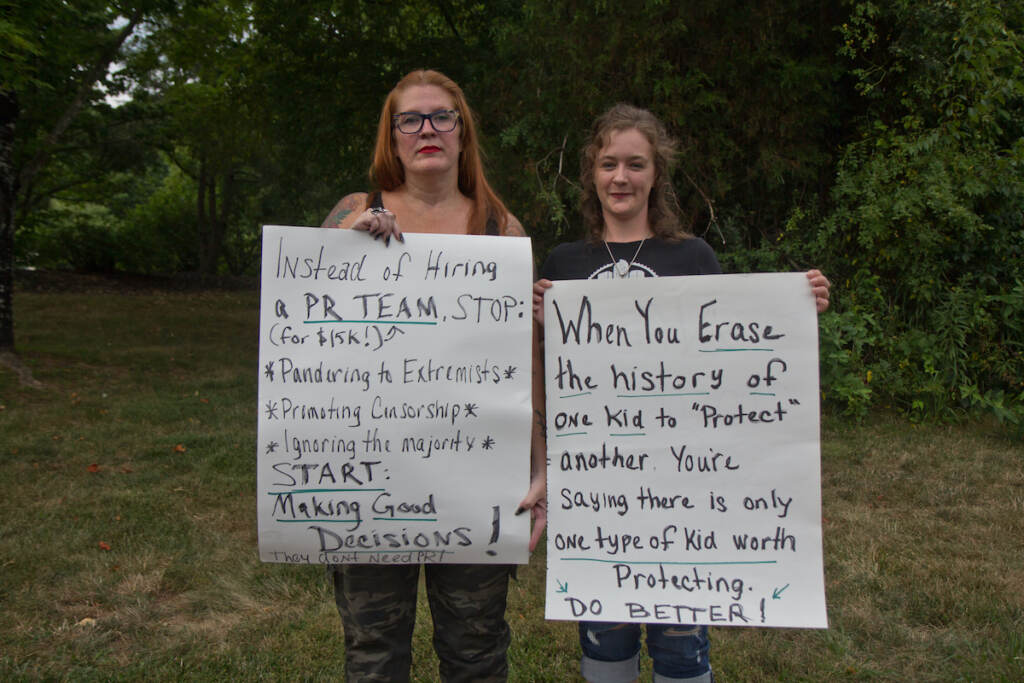 Michelle Wire and Lori Ary hold up signs at a rally against a library book policy at Central Bucks schools