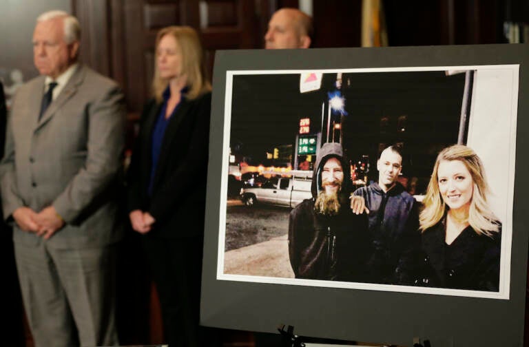 A photo of three people is displayed. People stand at attention behind it.