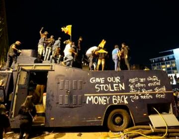 Protesters stand on a vandalised police water canon truck and shout slogans at the entrance to president's official residence in Colombo, Sri Lanka, Saturday, July 9, 2022. (AP Photo/Eranga Jayawardena)