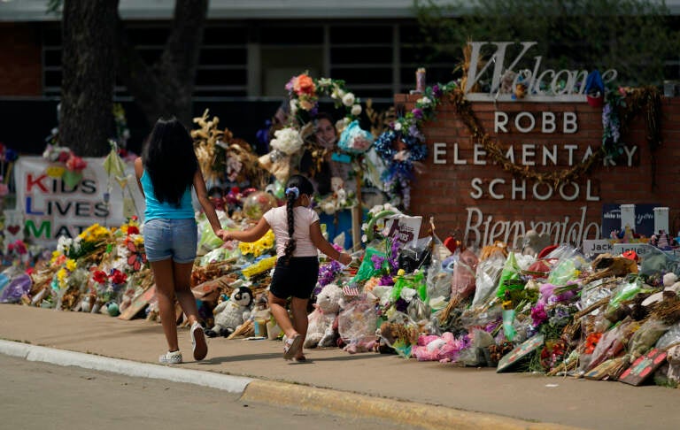 Visitors walk past a makeshift memorial honoring those recently killed at Robb Elementary School, Tuesday, July 12, 2022, in Uvalde, Texas. (AP Photo/Eric Gay)