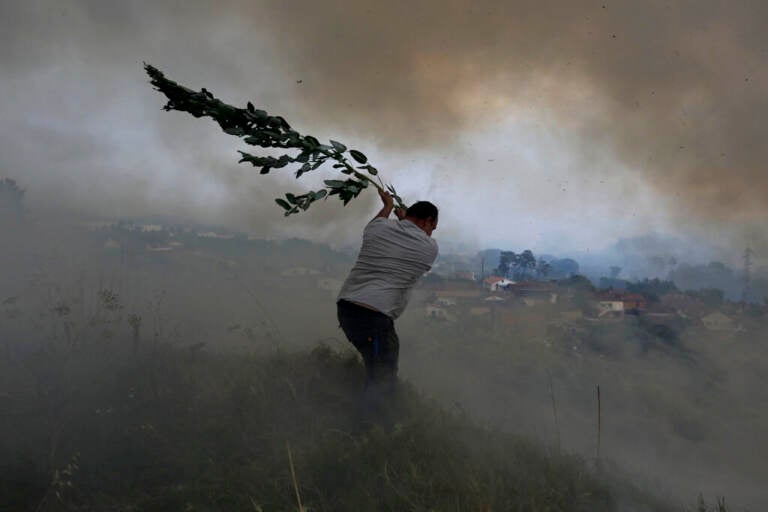 A volunteer uses a tree branch trying to prevent a forest fire from reaching houses in the village of Casal da Quinta, outside Leiria, central Portugal, Tuesday, July 12, 2022. (AP Photo/Joao Henriques)