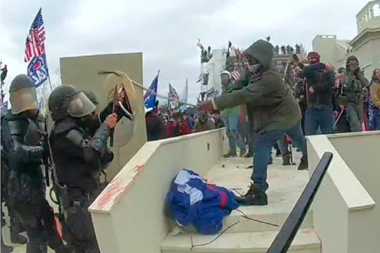 In this image from a Washington Metropolitan Police Department officer's body-worn video camera, and contained in the statement of facts supporting an arrest warrant for Mark Ponder, Ponder strikes an officer with a pole on the West Front of the U.S. Capitol on Jan. 6, 2021, in Washington. (Department of Justice via AP)