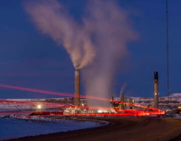 Smoke rises from a power plant, as the lights glow red in a snowy landscape at night.